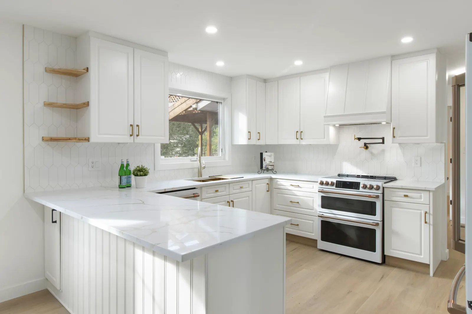 White Calgary kitchen with herringbone backsplash, quartz countertops, brass hardware, double wall oven and wood shelves.